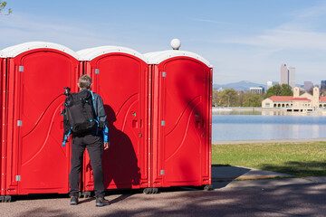 Red portable restrooms along a lakefront path with the skyline behind